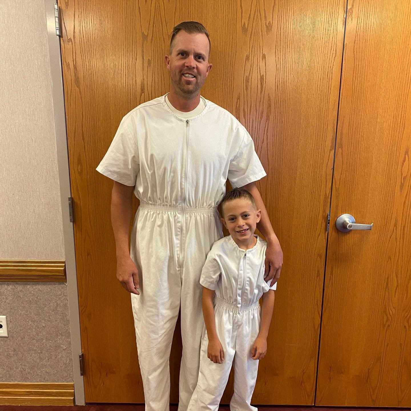 Fire Captain Spencer Long wraps his arm around one of his young sons, both wearing matching, full-body white zippered outfits. This proud father-son moment shows the quiet and guiding influence Spencer had in his family's lives.