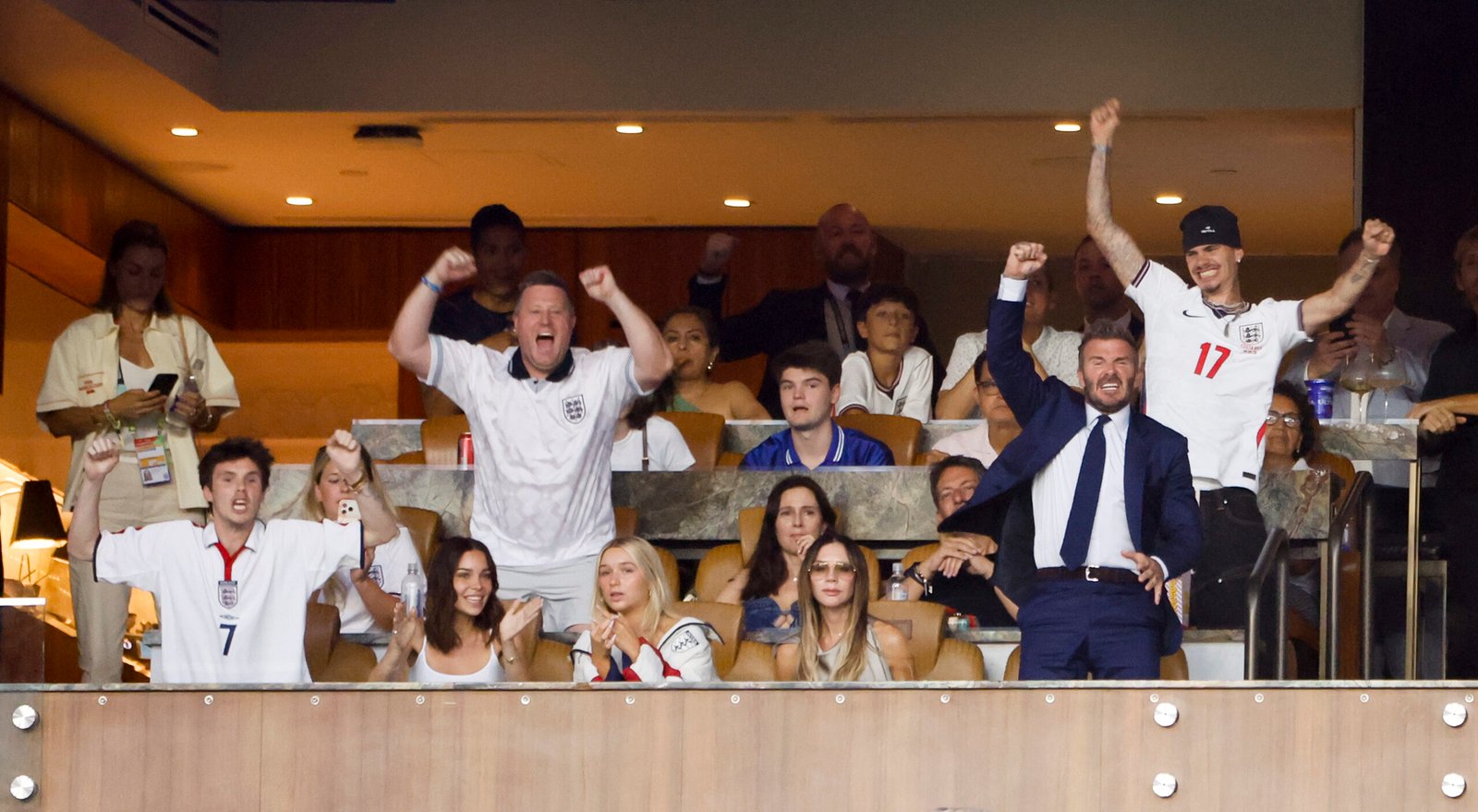 David, Victoria, Cruz, and Romeo Beckham cheer energetically during a high-stakes moment of the soccer tournament, fully immersed in the action of football's biggest night in a luxury stadium suite.