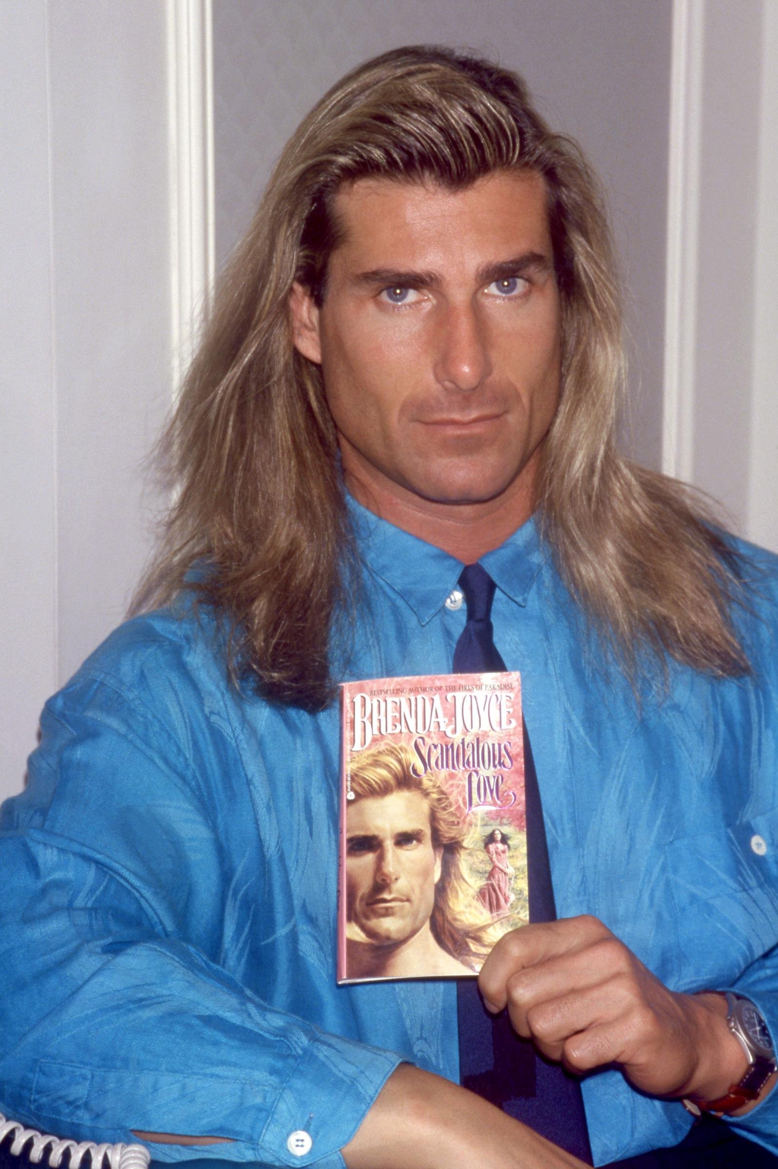 But he would soon find his fame in the most unexpected place. In this photo, the iconic romance book cover star posed for a portrait with Brenda Joyce's book "Scandalous Love" in New York, New York, on November 8, 1992.