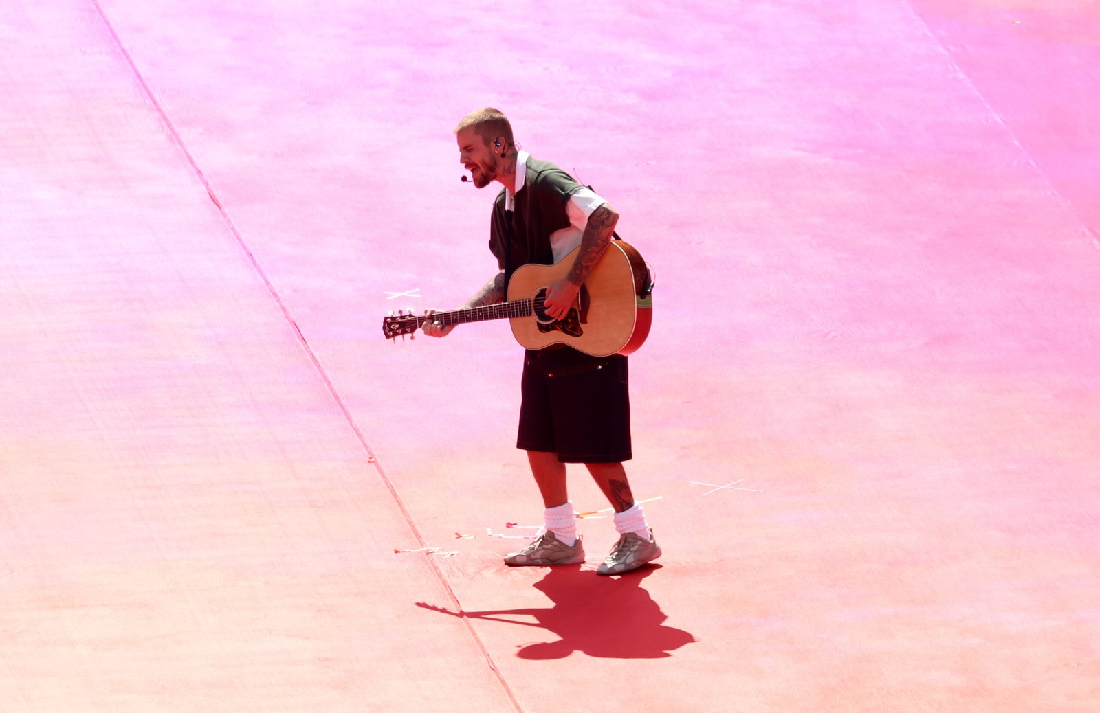 Justin Bieber is captured from a high angle during his Topps Final Halftime Show set, crooning with his guitar against a vibrant, pink-hued stage floor at MetLife Stadium.